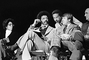 Photo of Jesse Jackson and mayor sitting, surrounded by 3 other unidentified people