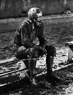Photo of football player sitting on sidelines covered head to toe in mud