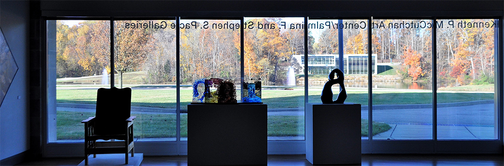 Picture of various pieces of art in front of window of gallery, overlooking reflection lake