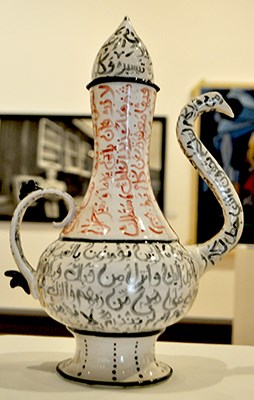 Ceramic pitcher with long spout. Painted white with red and black lettering, possibly arabic. Sarah Alsaied, Traditions
