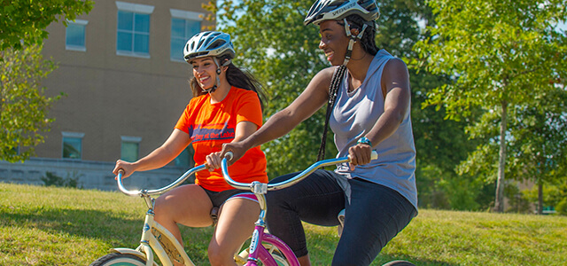 two students, wearing helmets, riding rental bikes along USI boulevard