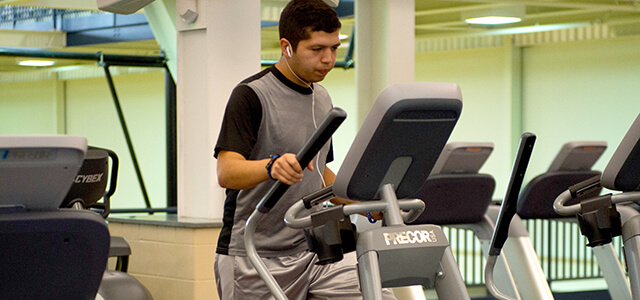 Student with ear buds in, on cardio equipment in fitness center