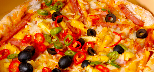 Pizza covered in various toppings such as olives, peppers, pineapple