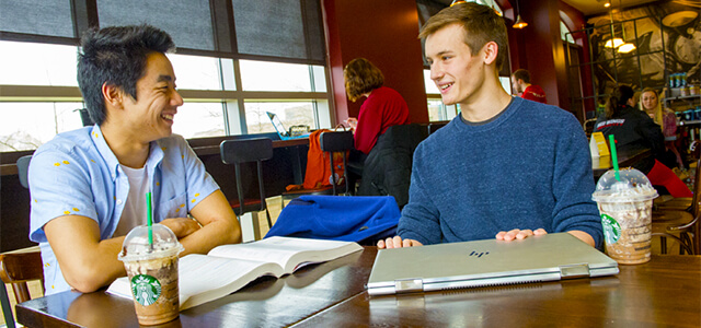 Two students, sitting at Starbucks, laughing while studying with Starbucks cups nearby