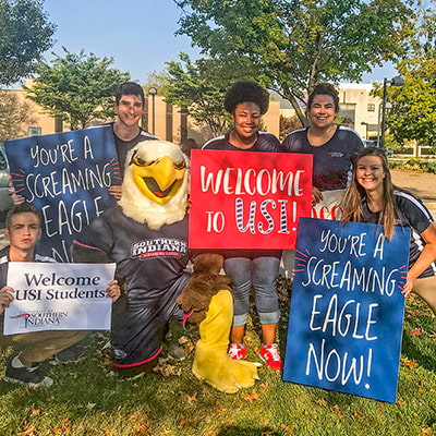 Students posing with Archie, holding 'Welcome to USI' signs