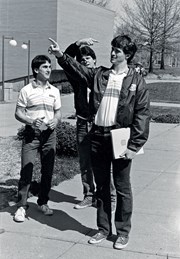 caption contest image of three students standing on USI's campus, two of the students are pointing in opposite directions