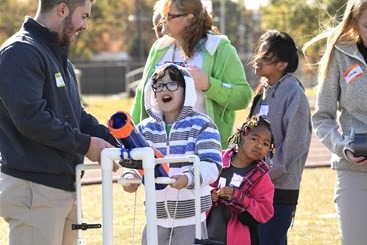 A USI OT student helps an EVSC student use a piece of adaptive equipment during the EVSC Special Olympics Unified Champions Game Day