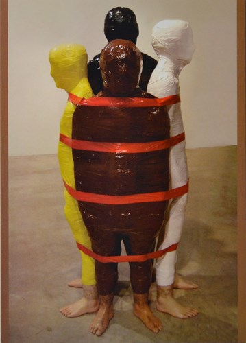 image and barefoot figures wraped in yellow, black, brown, white, and red tape