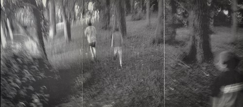 black and white photo of two people walking in the woods