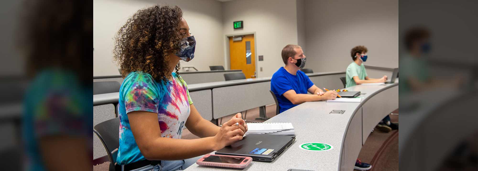 Students with masks sit in class listening to a professor