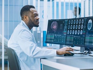 Man in lab coat sits in front of computer looking at brain scans