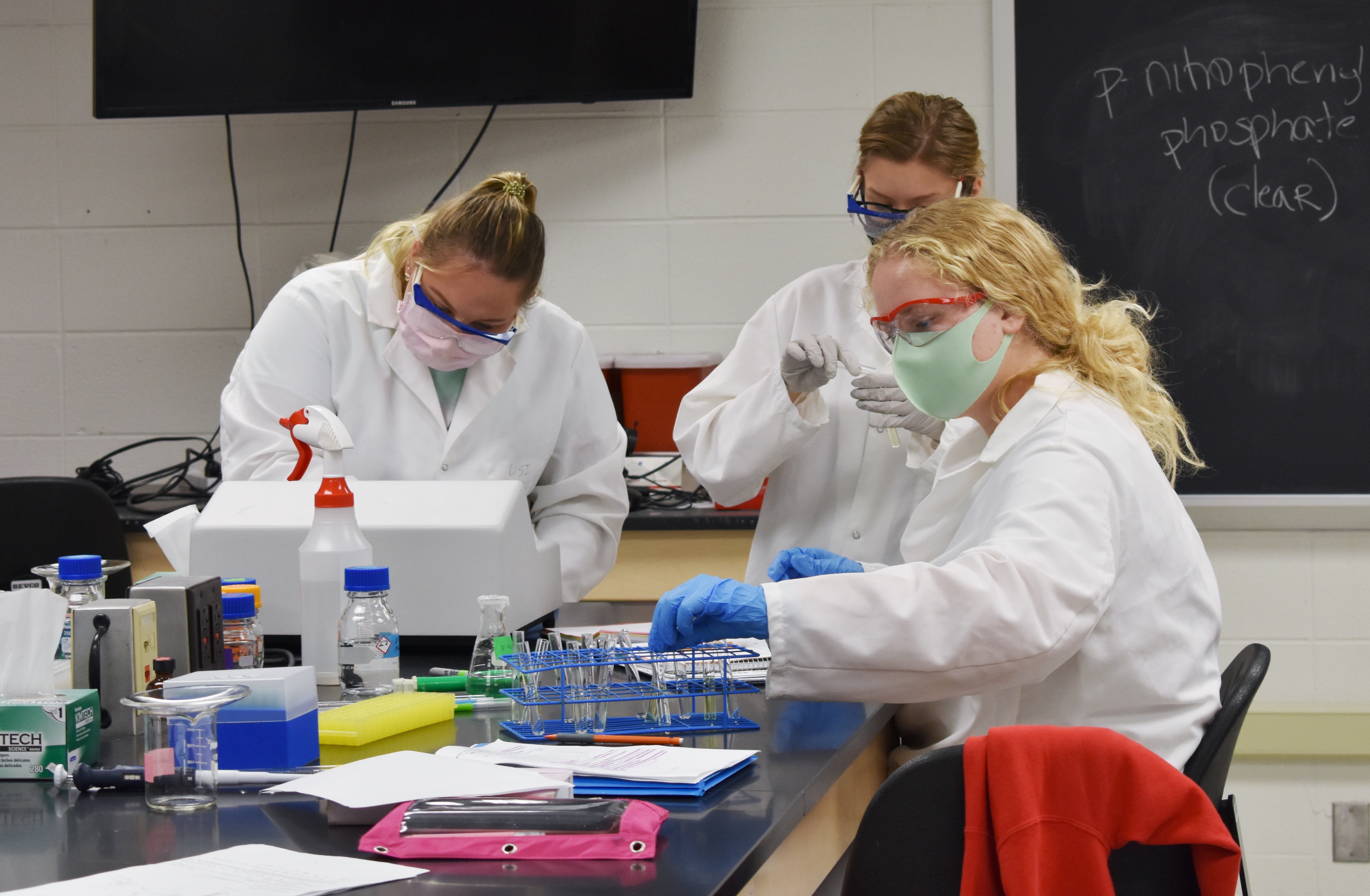 Introductory Biology Students in lab coats and goggles use a spectrophotometer to measure the optical density of samples.